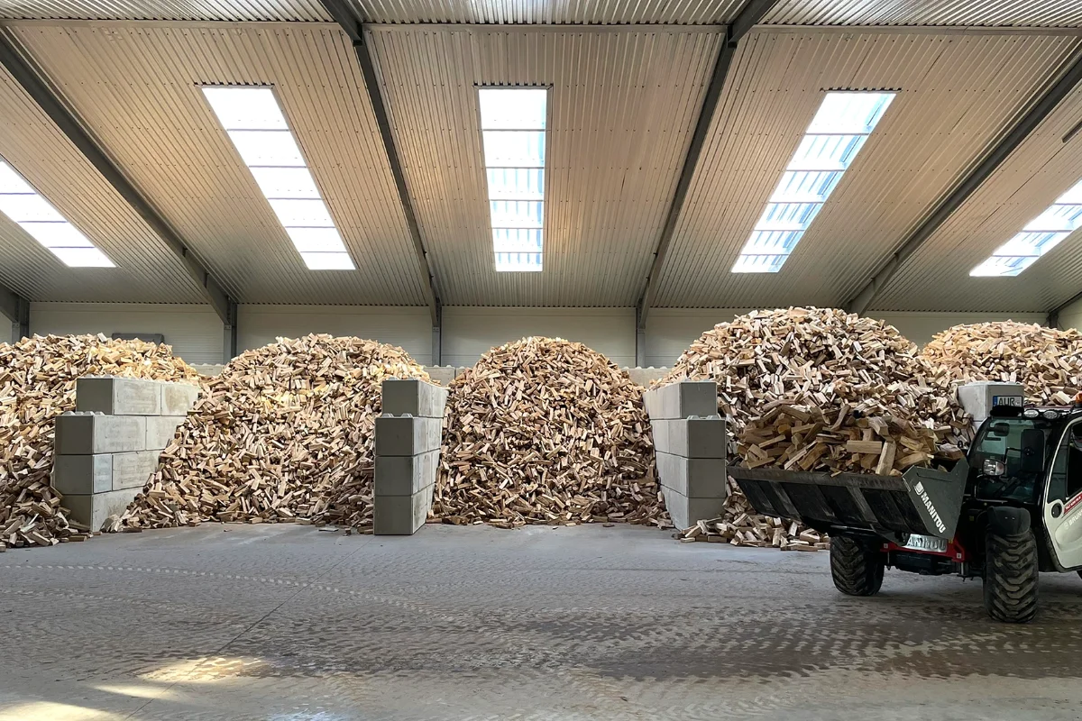 Lagerhalle mit aufgeschüttetem Brennholz und Anhänger